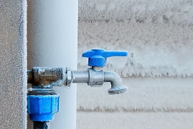 Frozen outdoor water spigot and pipe covered in ice and frost