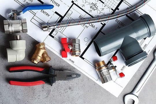 Plumbing tools, valves, and pipe fittings laid out on a house blueprint