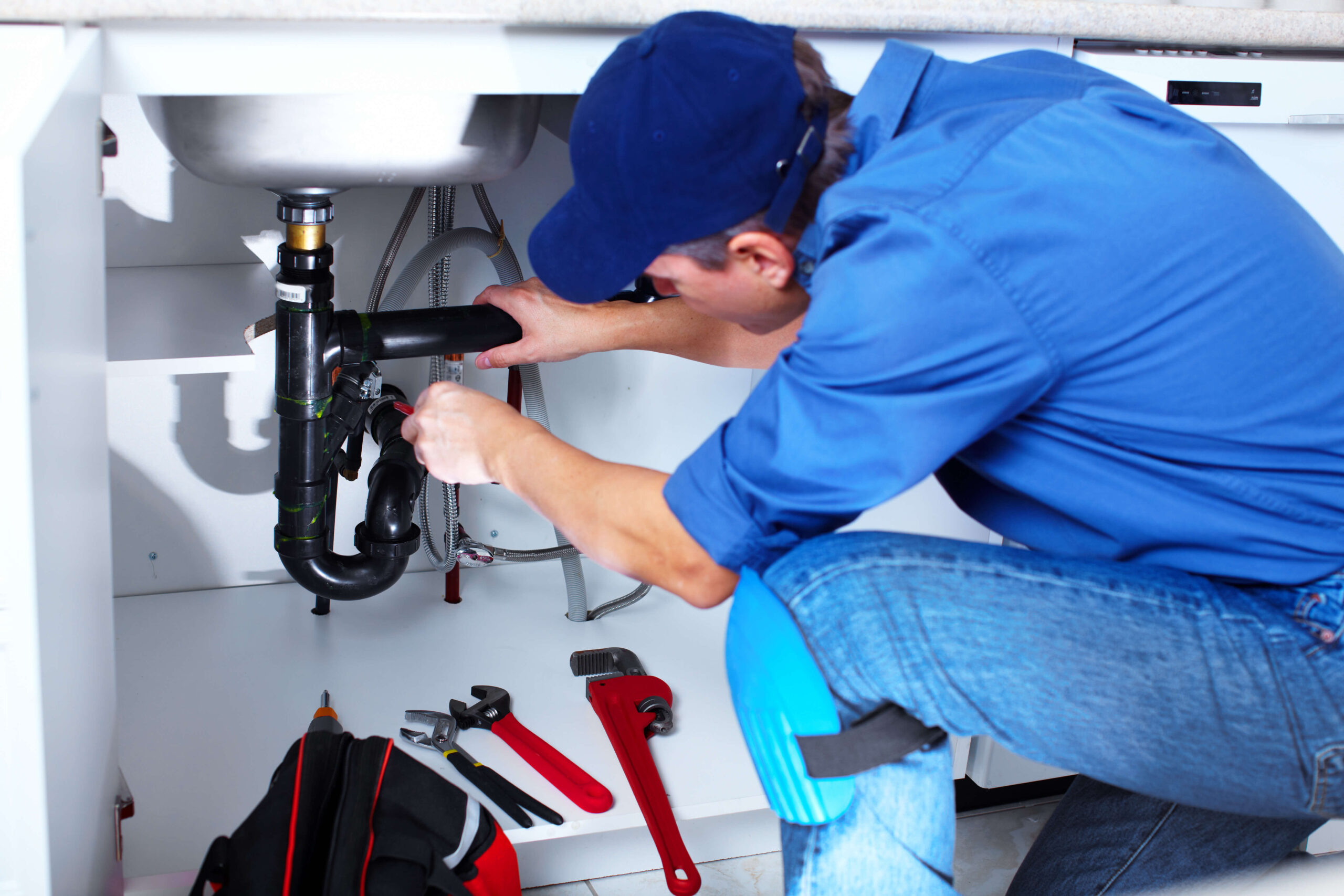 Licensed plumber repairing pipes under a kitchen sink with wrench and tools